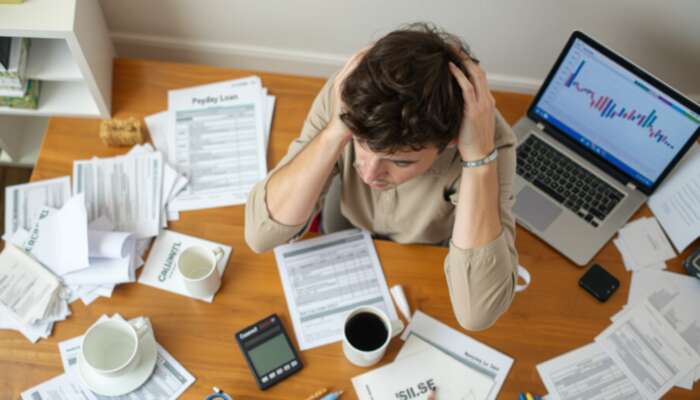 A stressed individual at a cluttered table with bills and a payday loan document, surrounded by empty coffee cups and a calculator, illustrating the challenges of high-interest debt and the need for financial alternatives.