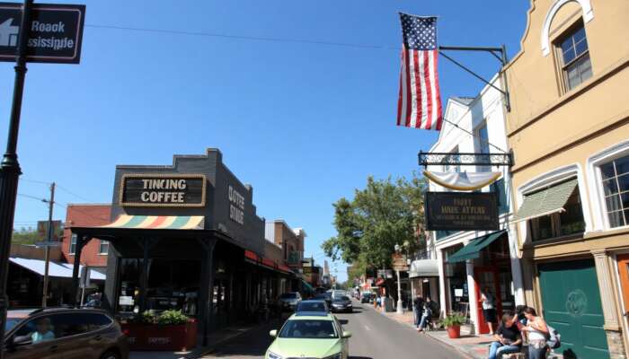 A cozy coffee shop on a busy urban street in Mississippi, with people enjoying drinks outside amidst charming storefronts and greenery under a bright blue sky.